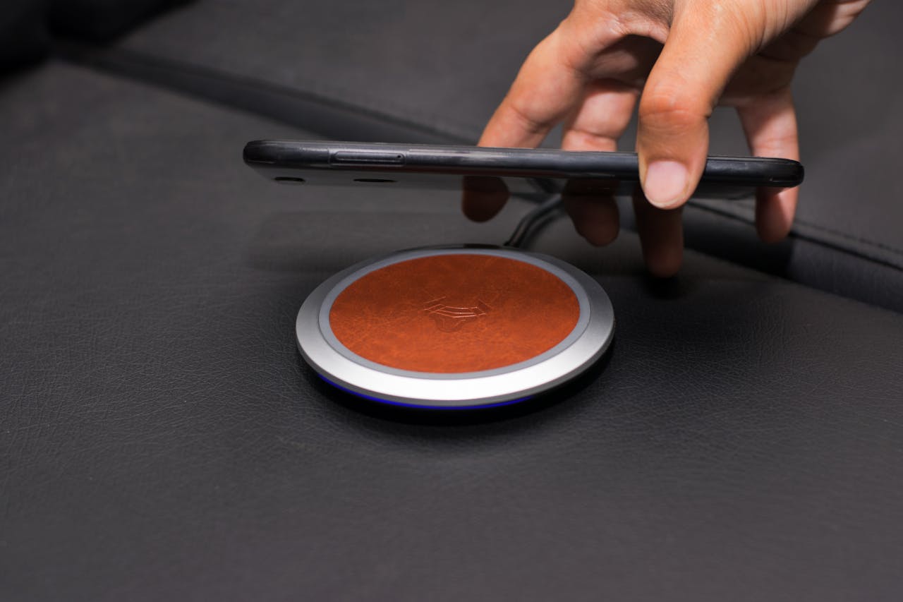 about-us Close-up of a hand placing a smartphone on a wireless charging pad on a leather surface.